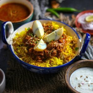Close-up of flavorful Indian biryani with boiled eggs, curry, and yogurt side dish.